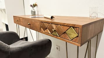 Un bureau en bois avec des tiroirs, un vase rempli de fleurs et un verre posé sur le bureau.