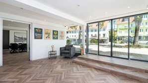 A modern interior with a herringbone wood floor, a grey armchair, and a dining area with black chairs. - Hotel Das Q Spaichingen (Spaichingen)