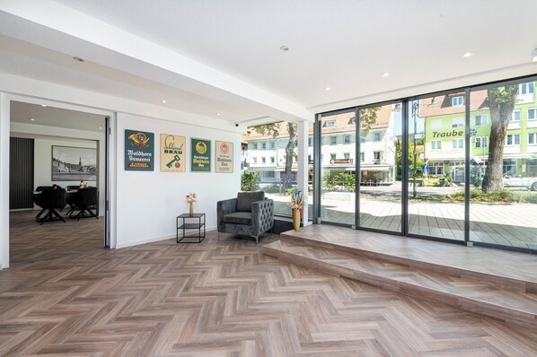 Un interior moderno con suelo de madera en espiga, un sillón gris y una zona de comedor con sillas negras.
