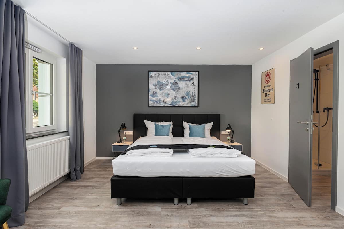 Un dormitorio moderno con una cama grande, mesitas de noche, una obra de arte enmarcada, un radiador y una puerta a la zona de la ducha.