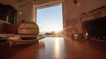 Un coin repas avec vue sur le coucher de soleil par la fenêtre, une table avec des assiettes et des verres, et une cheminée.