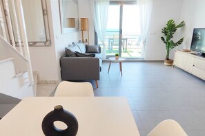 A modern living room with a sofa, a dining table, a TV, and a balcony with a plant.
