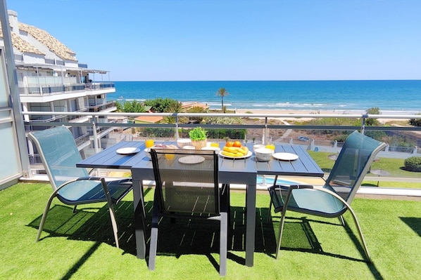 A balcony with a table set for two, overlooking a beach.