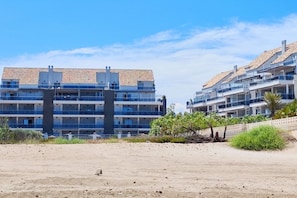 A coastal hotel with multiple-story buildings, balconies, and a sandy beach in the foreground.