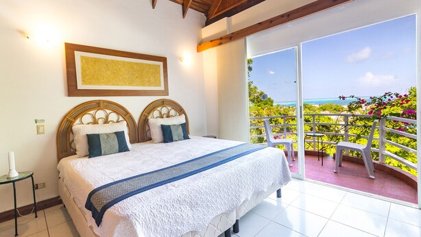 Een slaapkamer met een groot bed, een houten plafond, een ingelijst kunstwerk aan de muur en een balkon met uitzicht op zee.