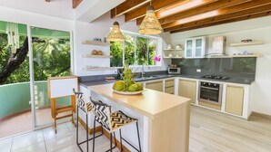 Een moderne keuken met een groot eiland, houten balken in het plafond en uitzicht op groen.