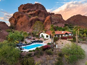A house with a pool, surrounded by desert vegetation and a large rock formation.
