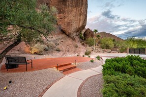 A park with a bench, a paved walkway, and a large rock formation.