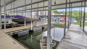 A covered dock area with boats, a waterway, and buildings in the background. - Waterfront Cozy Cove Retreat - LOTO Escape, Remodeled Comfort, Close to the Fun (Lake Ozark)
