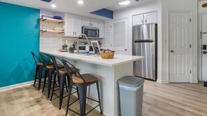 A modern kitchen with white cabinets, a stainless steel refrigerator, and a teal accent wall. - Waterfront Cozy Cove Retreat - LOTO Escape, Remodeled Comfort, Close to the Fun (Lake Ozark)
