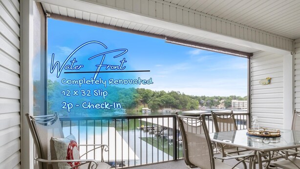A balcony with a view of a lake, a table with chairs, and a sign indicating a 12 x 32 slip area. - Waterfront Cozy Cove Retreat - LOTO Escape, Remodeled Comfort, Close to the Fun (Lake Ozark)