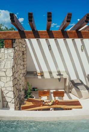 Un espace extérieur ensoleillé, aménagé avec une terrasse, un mur en pierre, une pergola en bois et une piscine.
