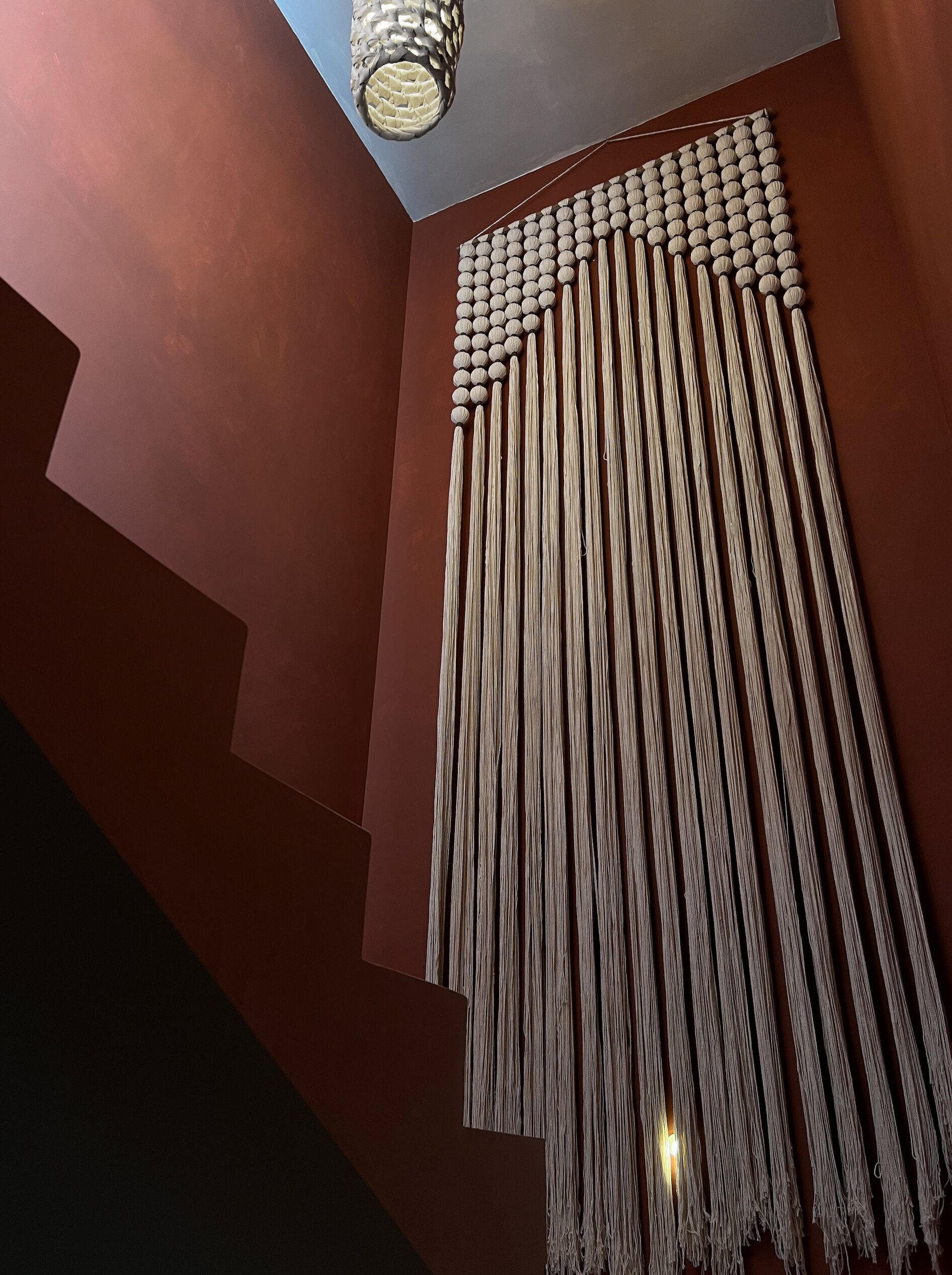 A modern interior with a staircase, a hanging macramé wall, and a ceiling light fixture.
