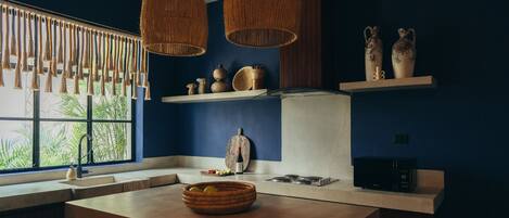A kitchen with a large window, wooden counter, hanging wicker light fixtures, and a bowl of fruit.