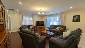 A living room with two sofas, a coffee table, and a TV. There is a wooden cabinet and a chandelier. - Home with easy access to CBD: Magill (Magill)