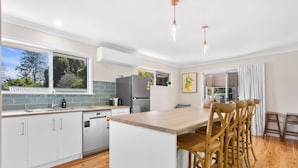 A modern kitchen with white cabinets, a wooden countertop, and a central island with bar stools. - Maple Cottage -Perfect Eastside Location (East Toowoomba)