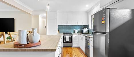 A modern kitchen with white cabinets, a black refrigerator, a wooden countertop, and a tiled backsplash.