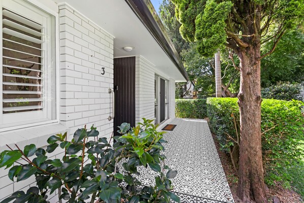 A house with white brick exterior, a dark door, and a tiled pathway leading to the entrance. - Maple Cottage -Perfect Eastside Location (East Toowoomba)