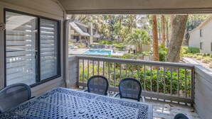 A balcony with a table and chairs, overlooking a swimming pool and neighboring houses.