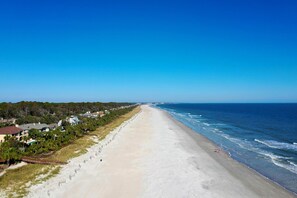 A long, sandy beach with ocean waves, lined with houses and greenery.