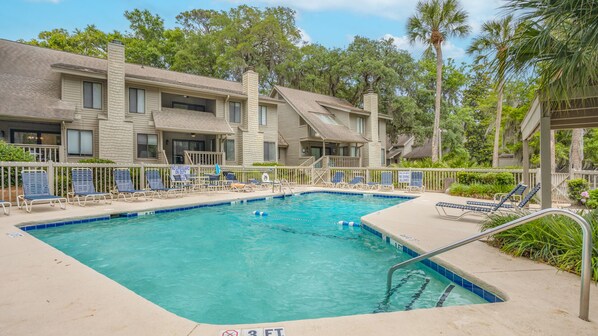 A swimming pool with lounge chairs, a lifeguard tower, and a building with balconies.