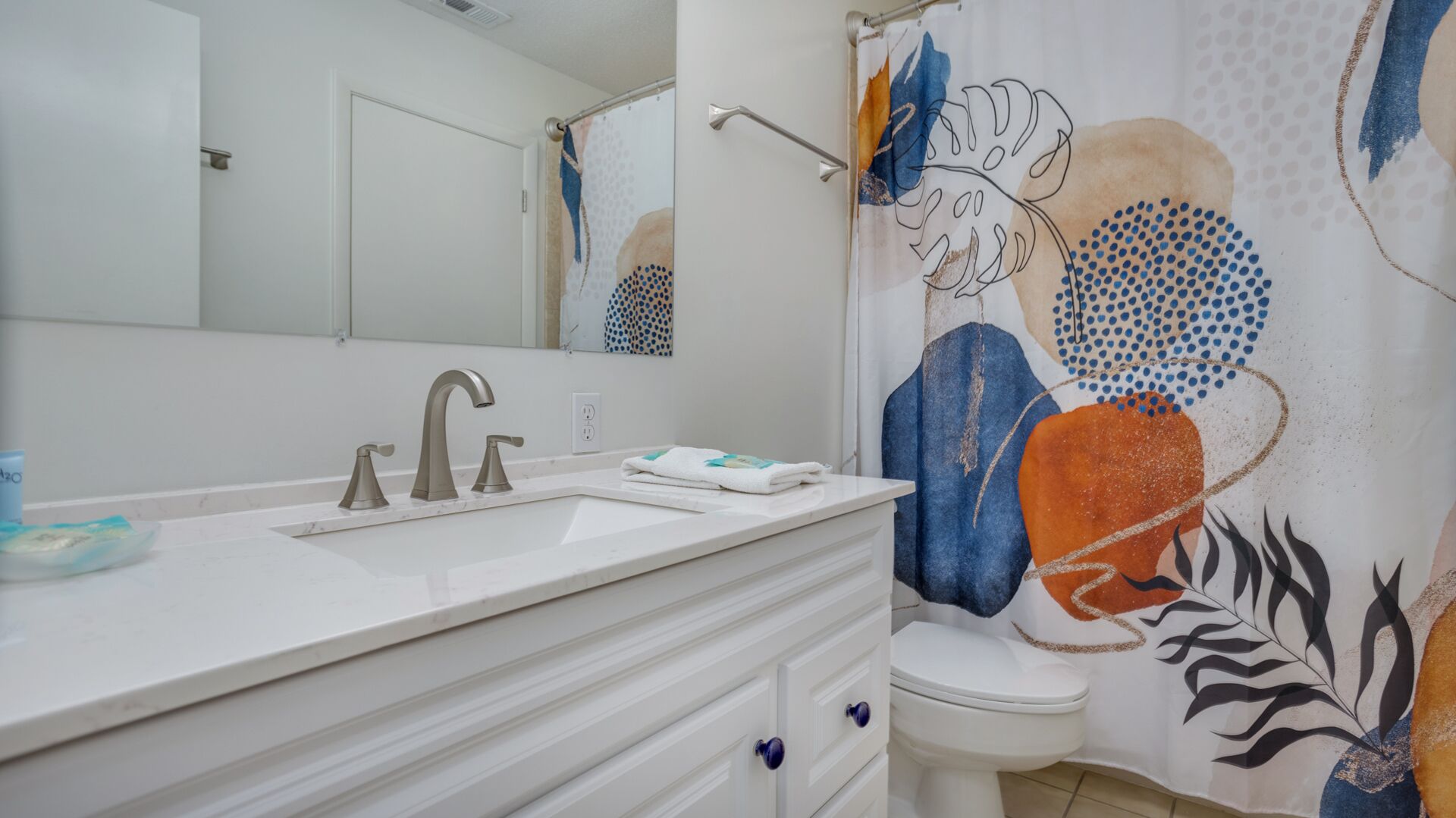 A bathroom with a white vanity, a sink with two faucets, a toilet, and a shower curtain with a floral pattern.