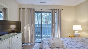 A hotel room with a bed, a TV on a dresser, a lamp, and a balcony with curtains.
