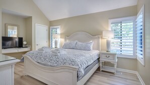 A bedroom with a large bed, bedside tables, a TV, and a window with blinds.