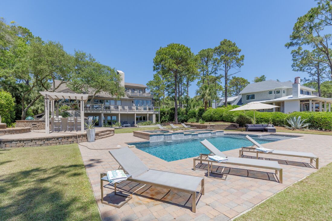A residential property with a swimming pool, outdoor seating, and a covered patio area.