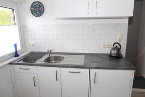 Une cuisine avec des meubles blancs, un évier en acier inoxydable, une bouilloire et une assiette décorative accrochée au mur.