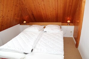 Un lit simple dans une chambre dont le plafond et les murs sont en bois, avec deux lampes de chevet et un sol recouvert d’une moquette.