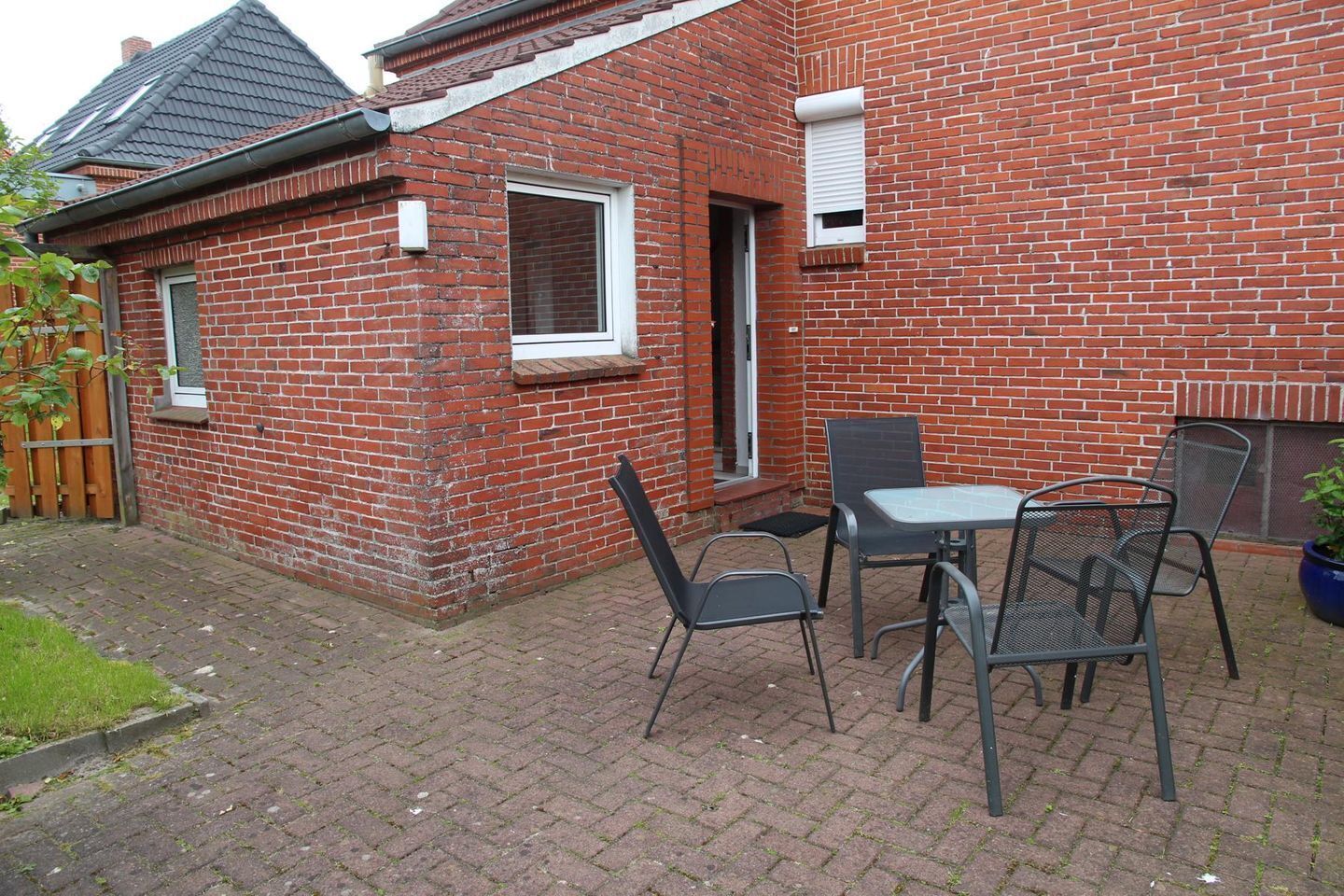 A brick house with a tiled roof, a window, and a door. There is a table and four chairs outside.