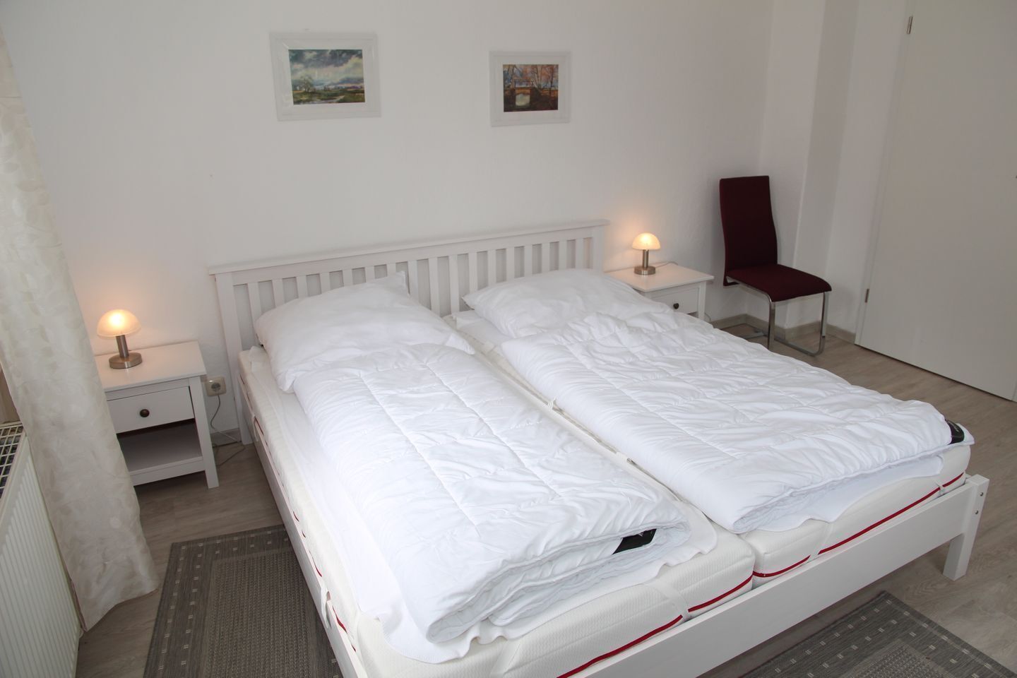 A double bed with white bedding, two bedside tables with lamps, and two framed pictures on the wall.