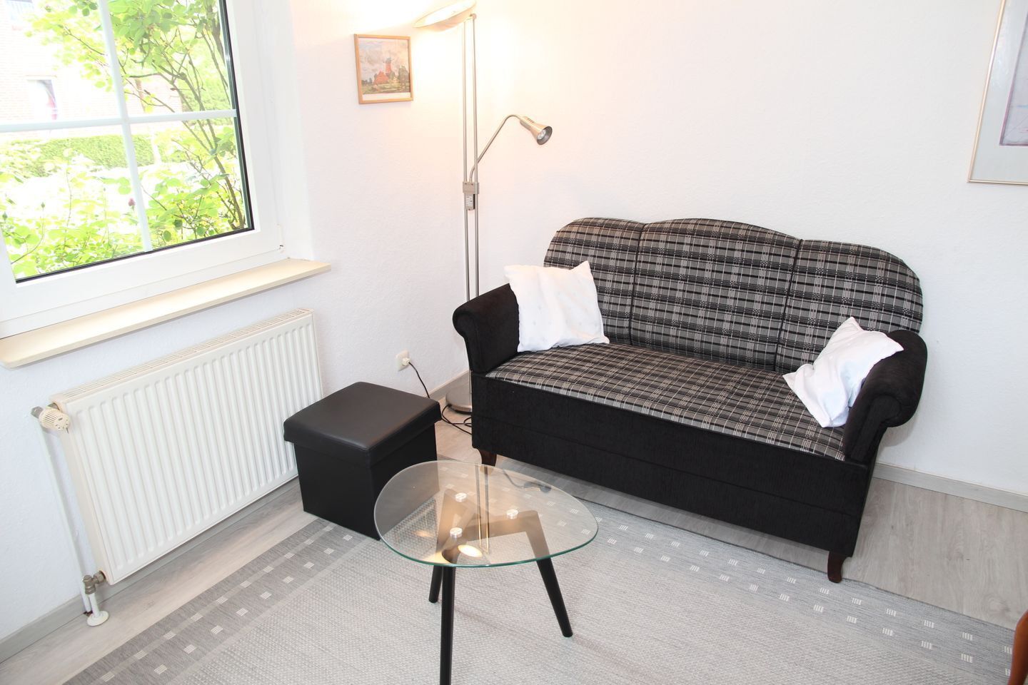 A cozy room with a plaid sofa, a glass coffee table, and a radiator.