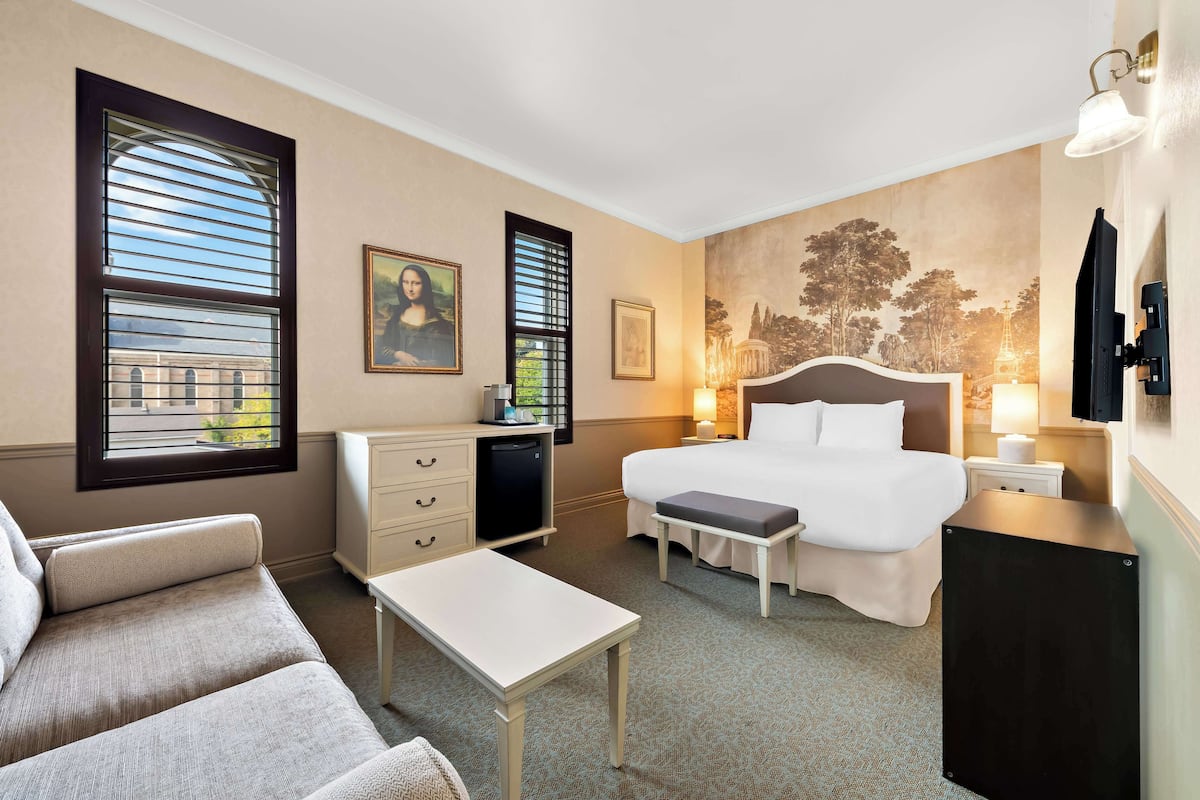 Habitación de hotel con cama, escritorio, silla, pequeña mesa, banco, cómoda y televisor.