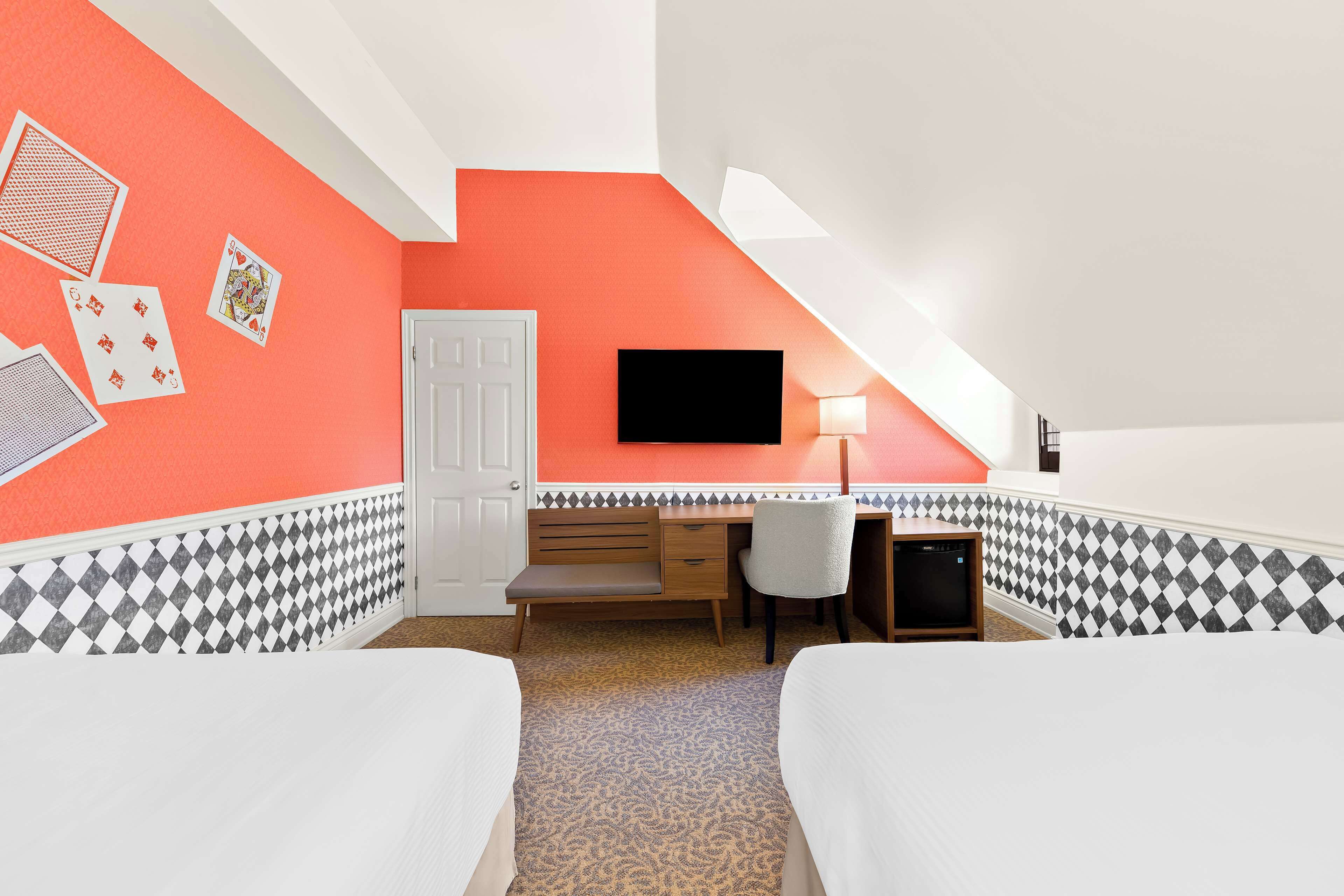 A room with a sloped ceiling, a desk with a chair, a television, and two beds.