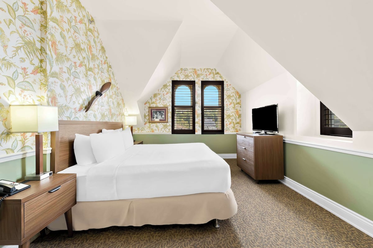 Habitación de hotel con cama, mesita de noche, lámpara, cómoda, televisor y ventana con vistas.