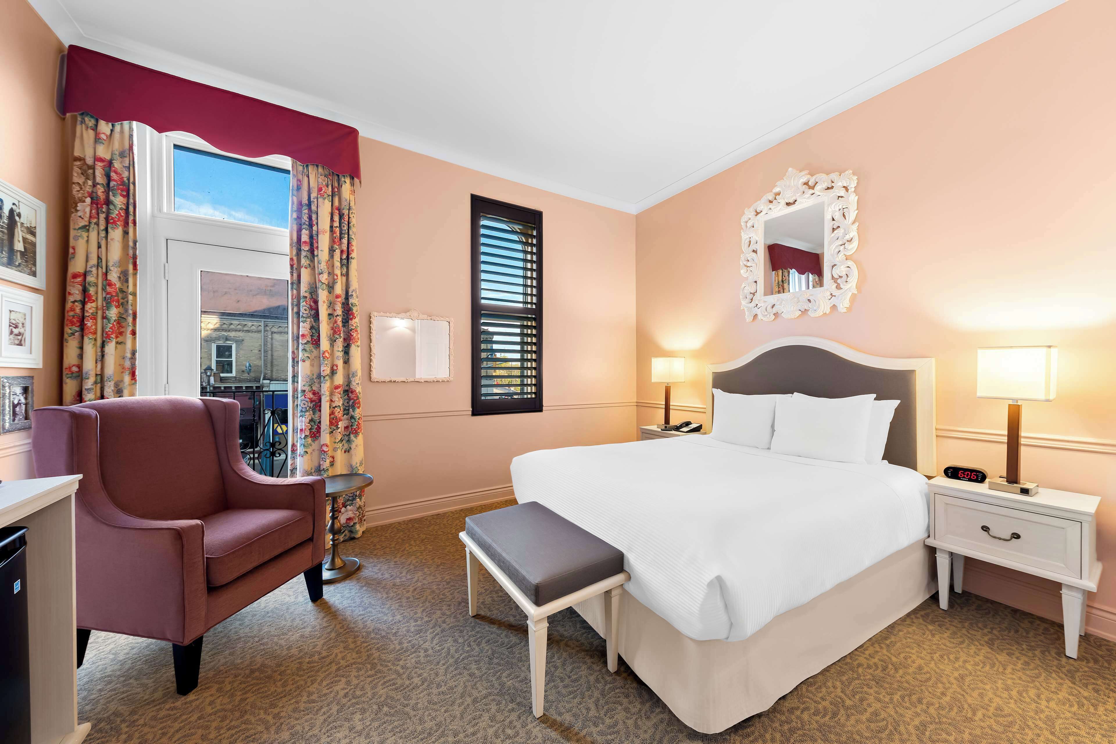 A hotel room with a large bed, a desk, a chair, a small table, and a window with curtains.
