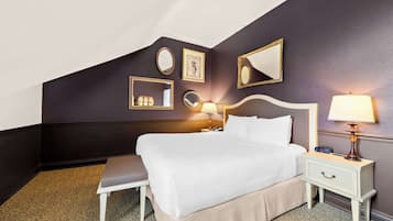 Habitación de hotel ordenada con una cama grande, mesitas de noche, un banco y espejos en la pared.