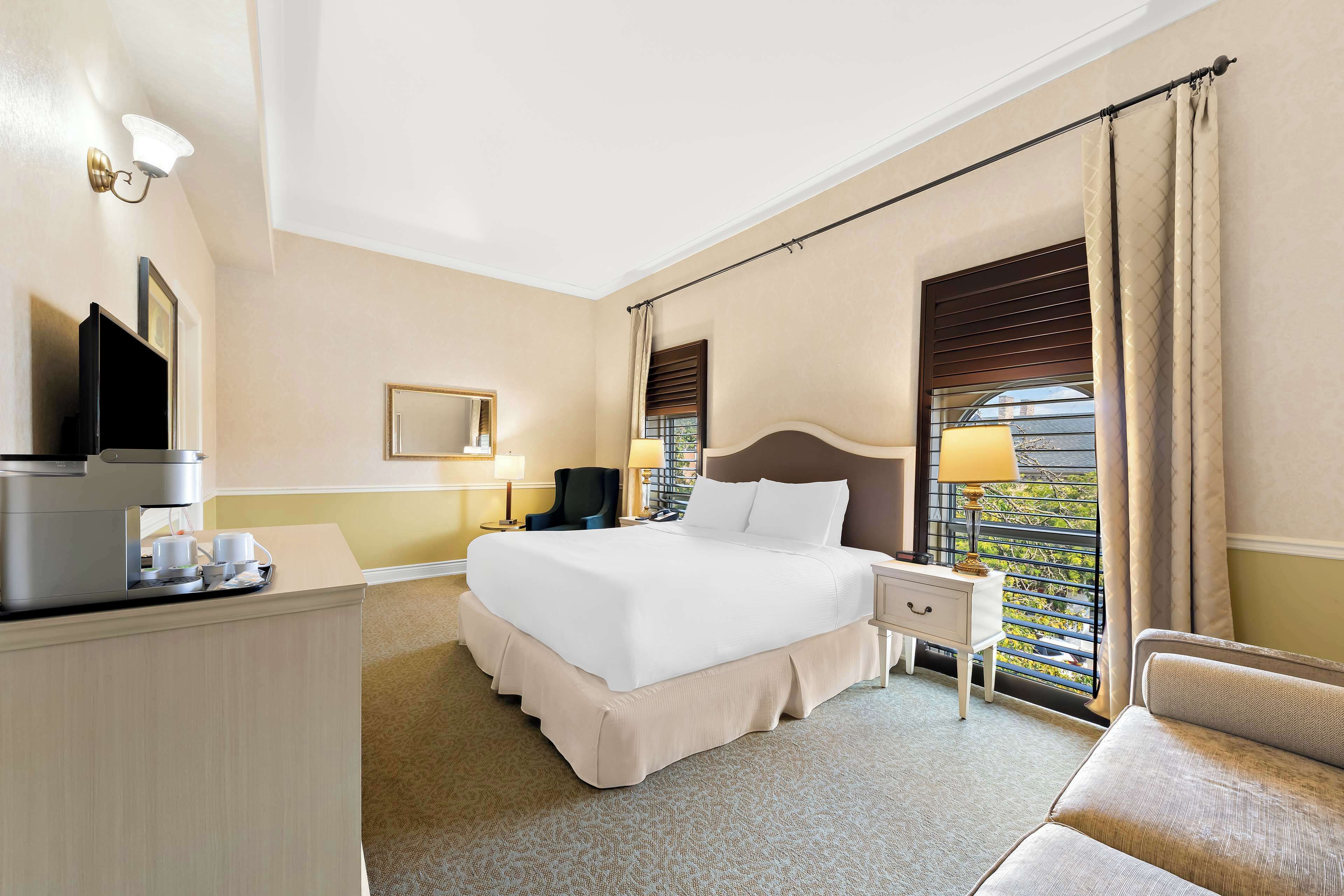 Een hotelkamer met een groot bed, een bureau met koffiezetapparaat, een stoel en een raam met gordijnen.