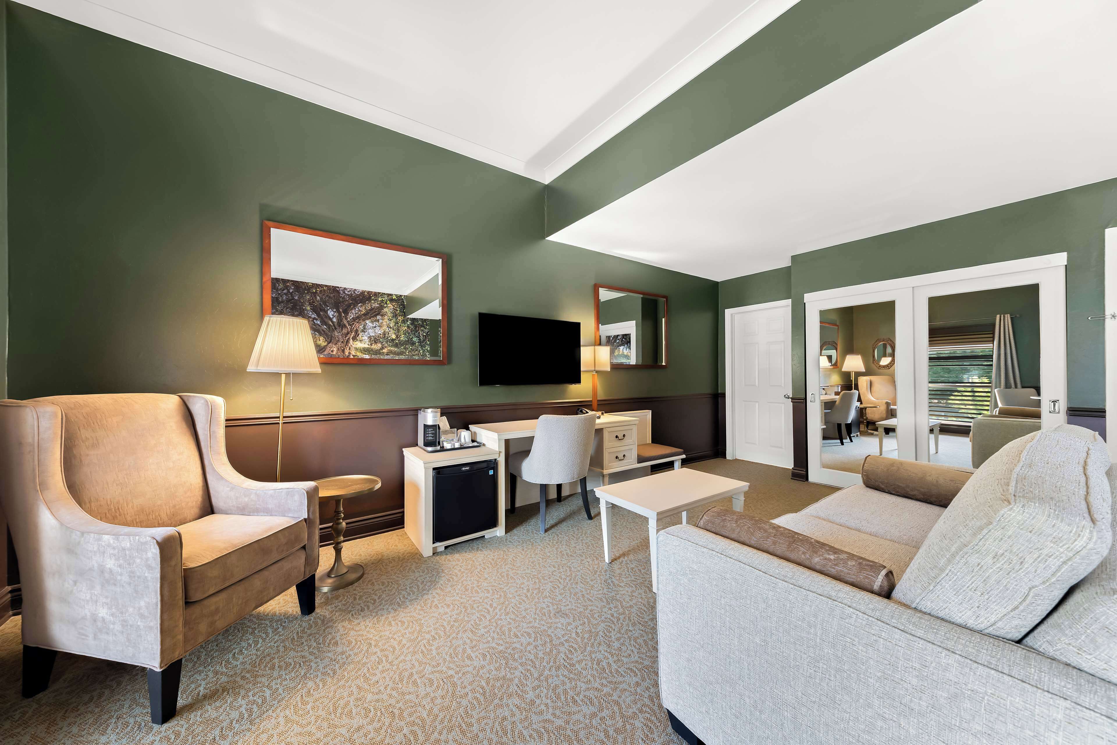 A hotel room with a sofa, armchair, desk, and a television.