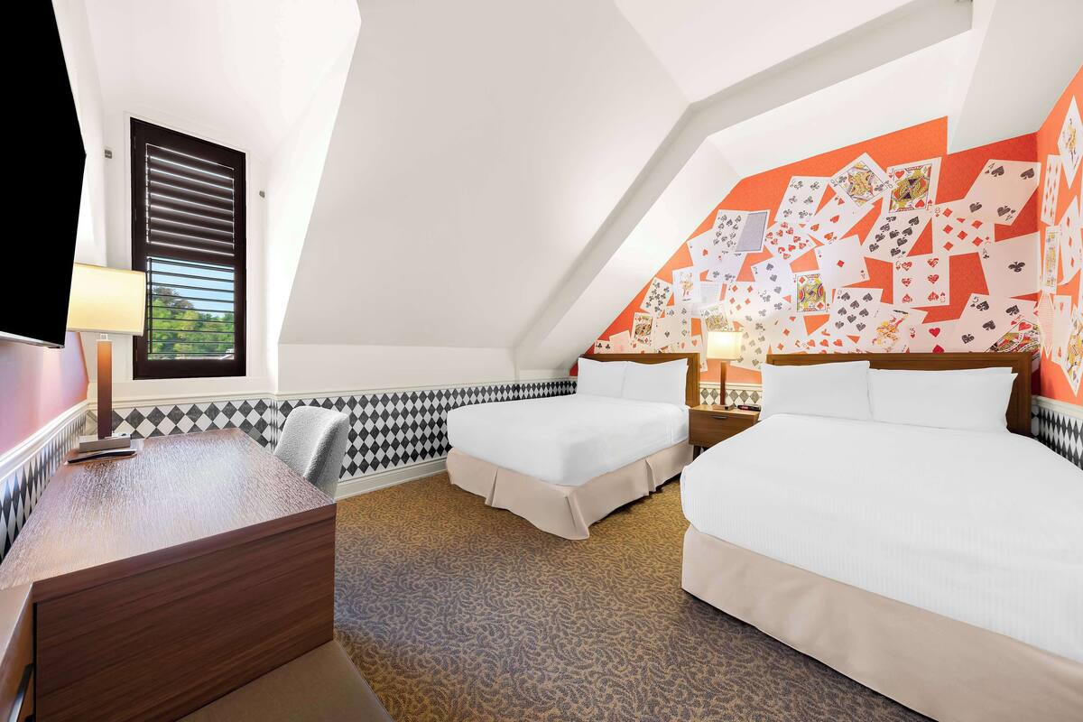 Habitación de hotel con dos camas, un escritorio y una alfombra estampada.