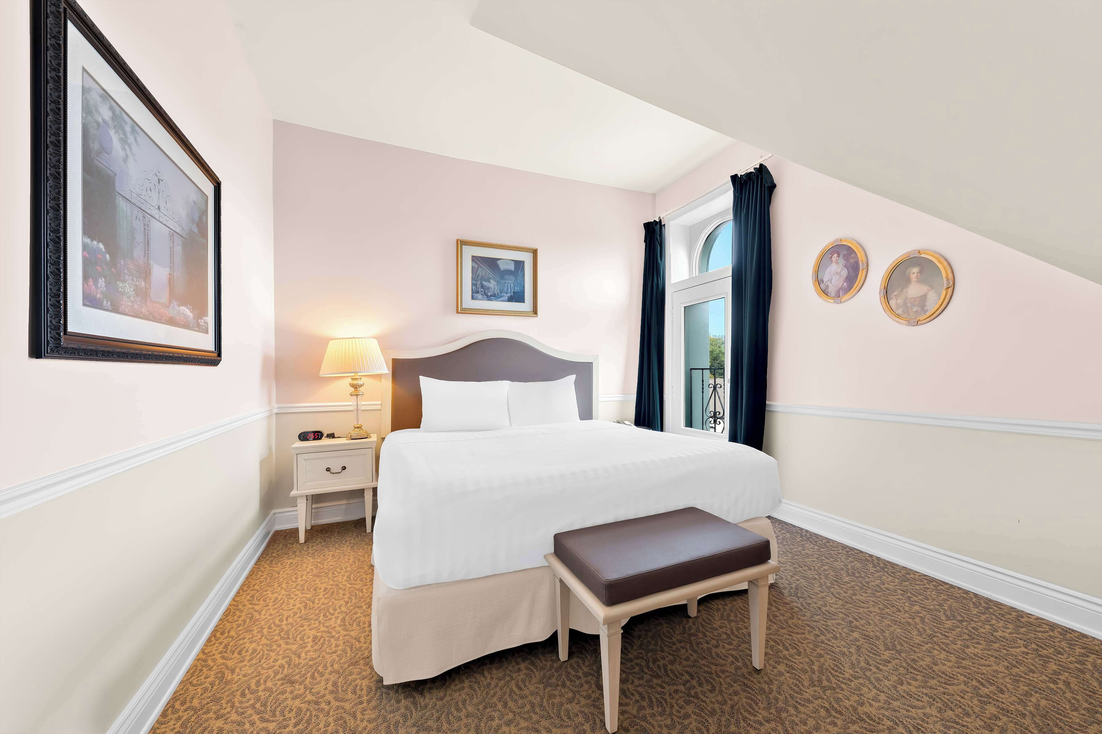 A neatly arranged hotel room with a bed, bedside table, lamp, and a bench.