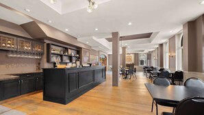 A spacious restaurant with a long counter, multiple tables, and a bar area with shelves and glasses. - The Arlington Hotel, Bw Signature Collection (Brant)