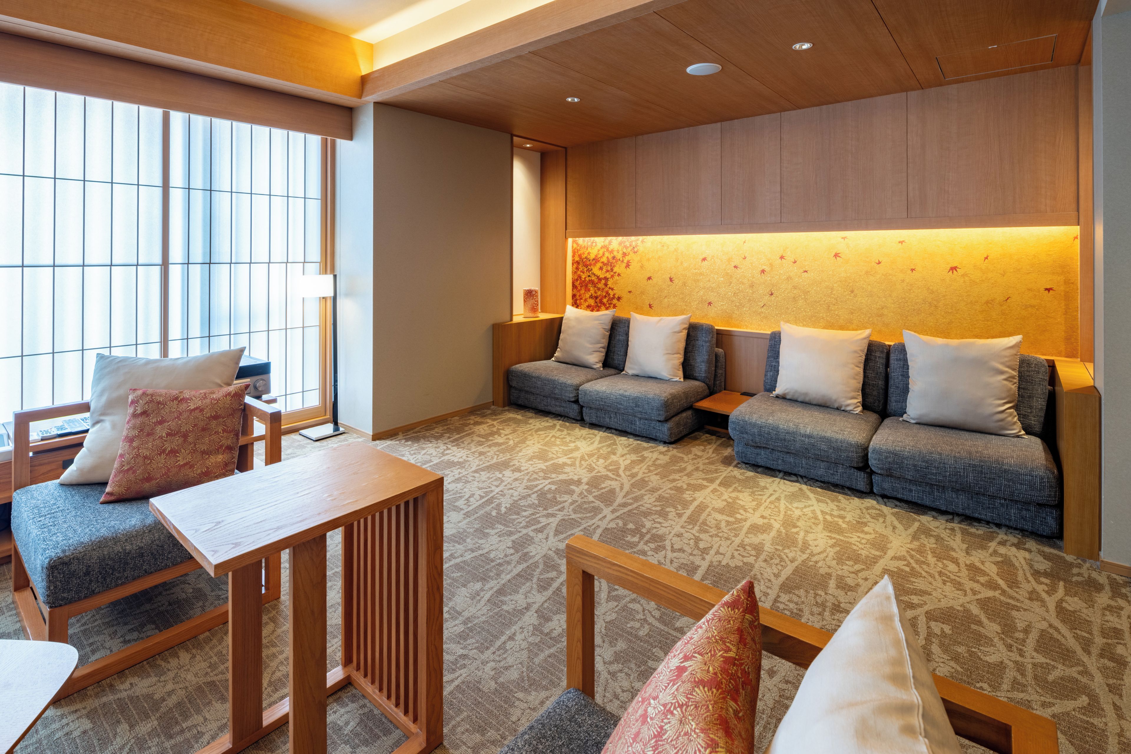 A modern hotel lobby with a seating area, a wooden reception desk, and a large window providing natural light.