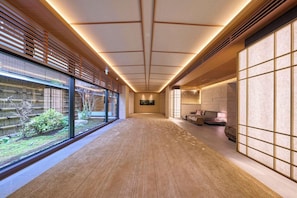 Un couloir avec des lambris en bois, une vue sur la verdure et un coin salon avec une lampe.