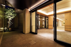 Une entrée moderne avec des portes en verre, un sol carrelé et un petit arbre à l’extérieur.