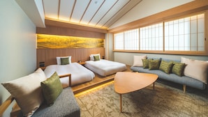 Une chambre d’hôtel moderne avec un canapé, deux lits, une tête de lit en bois et une grande fenêtre.