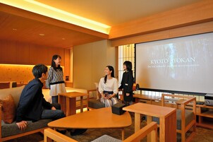 Eine Gruppe von Personen in einem modernen Innenraum mit Holzmöbeln und einer Projektionsleinwand, auf der 'KYOTO IYOKAN' zu sehen ist.