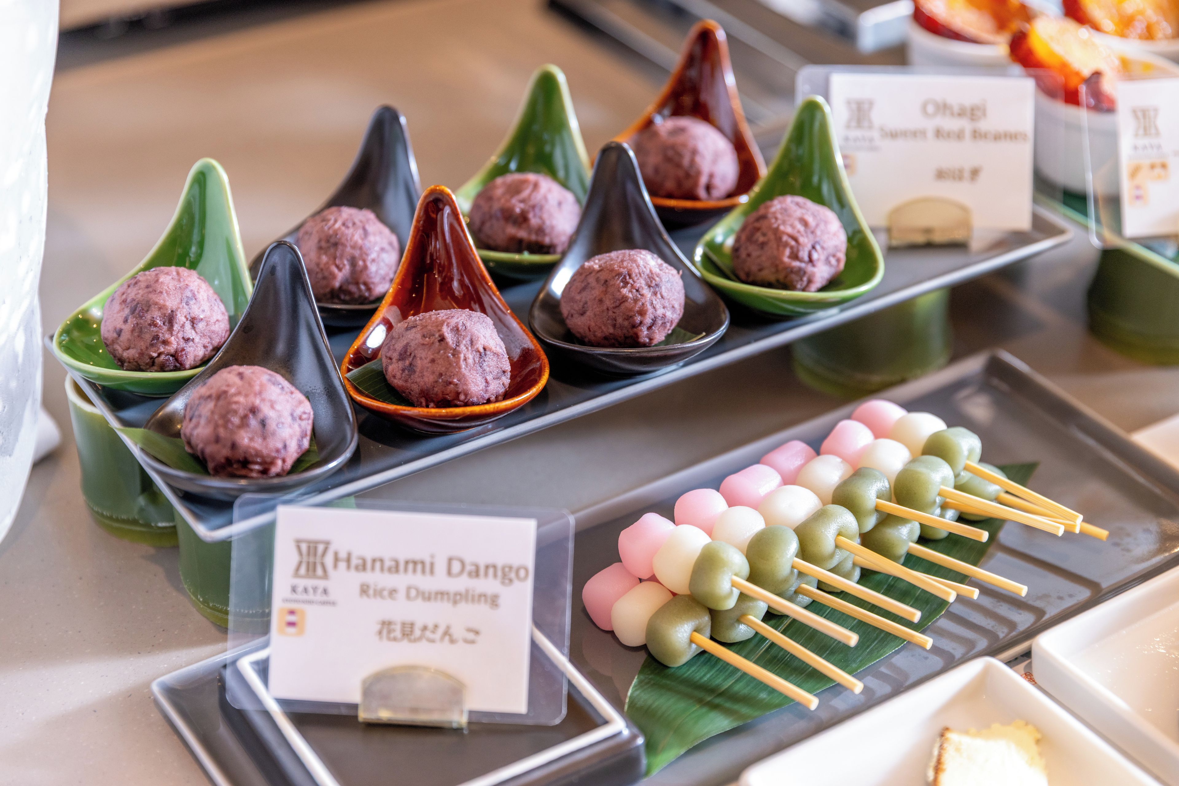A variety of food items displayed on a counter, including rice dumplings and skewered sweets.